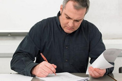 Caucasian man writing on white paper at desk